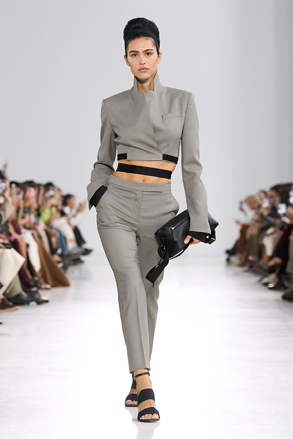 Défilé Max Mara Printemps Été 2026 : look tailleur gris avec veste et pantalon avec petit sac noir à la main.